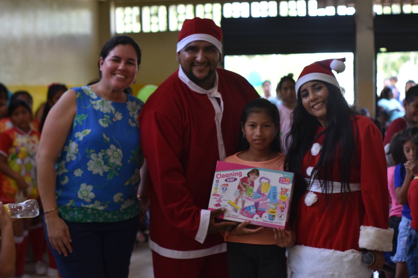 Niña recibiendo un regalo junto a la presidenta de la fundación y voluntarios